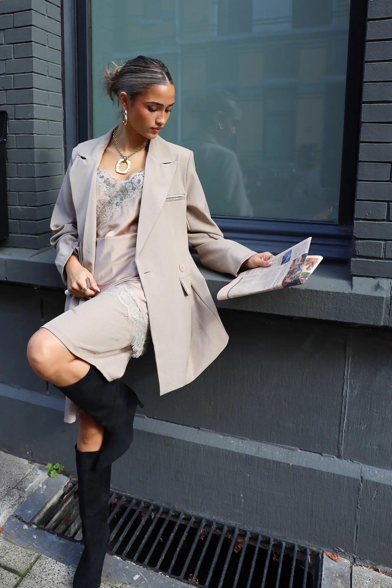 model zit op stoep met beige blazer over satijnen top en laarzen