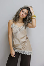 model draagt beige top met kant en bruine broek, hand in haar