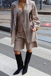 model met beige satijnen top, blazer en hoge laarzen op straat