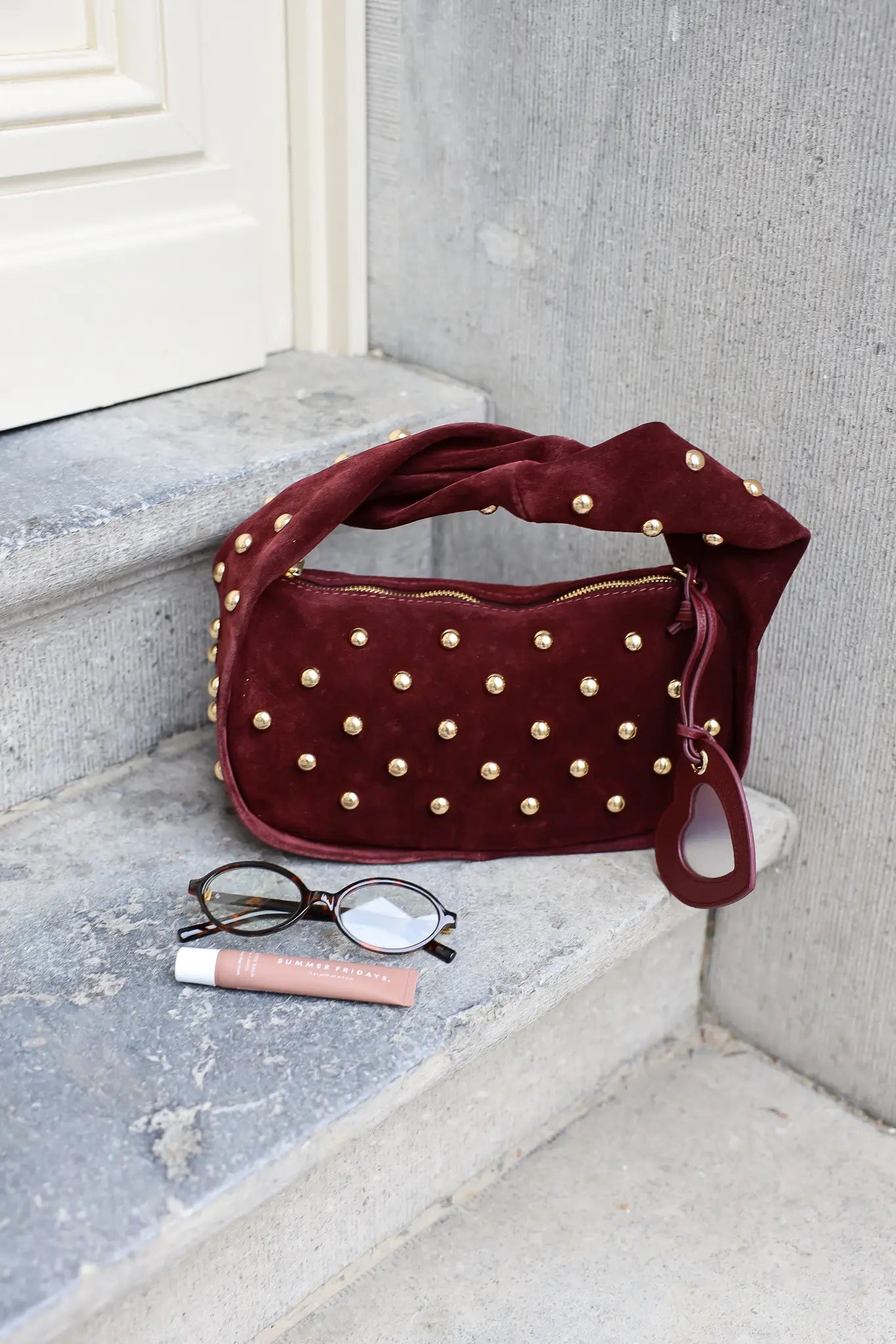 Bordeaux schoudertas met goudkleurige studs op een stenen ondergrond