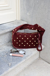 Bordeaux schoudertas met goudkleurige studs op een stenen ondergrond