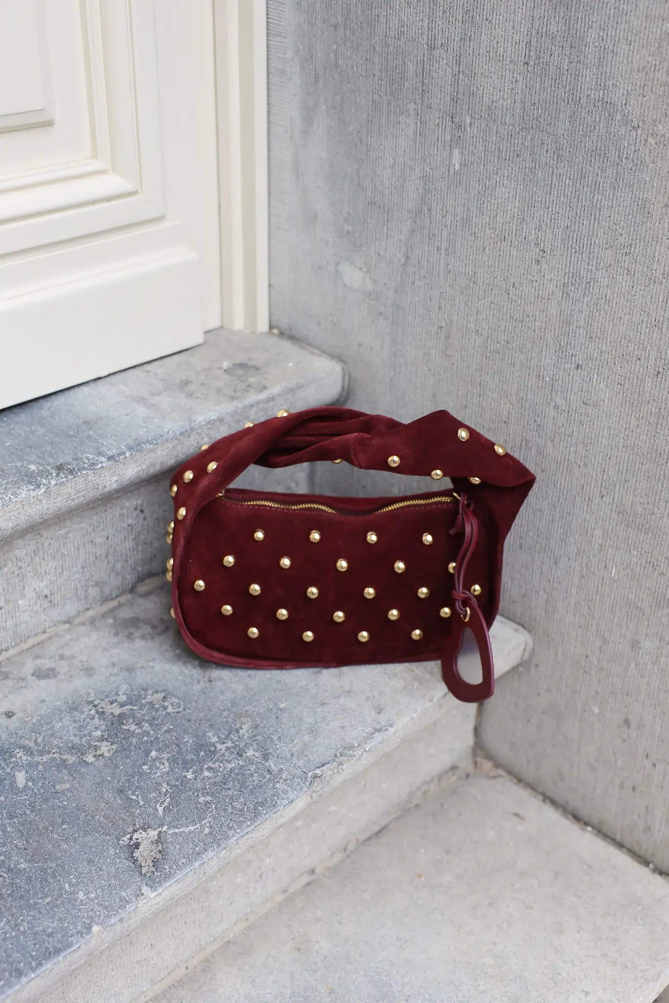 Zijaanzicht van bordeaux tas met studs en losse hartvormige spiegelhanger