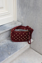 Zijaanzicht van bordeaux tas met studs en losse hartvormige spiegelhanger