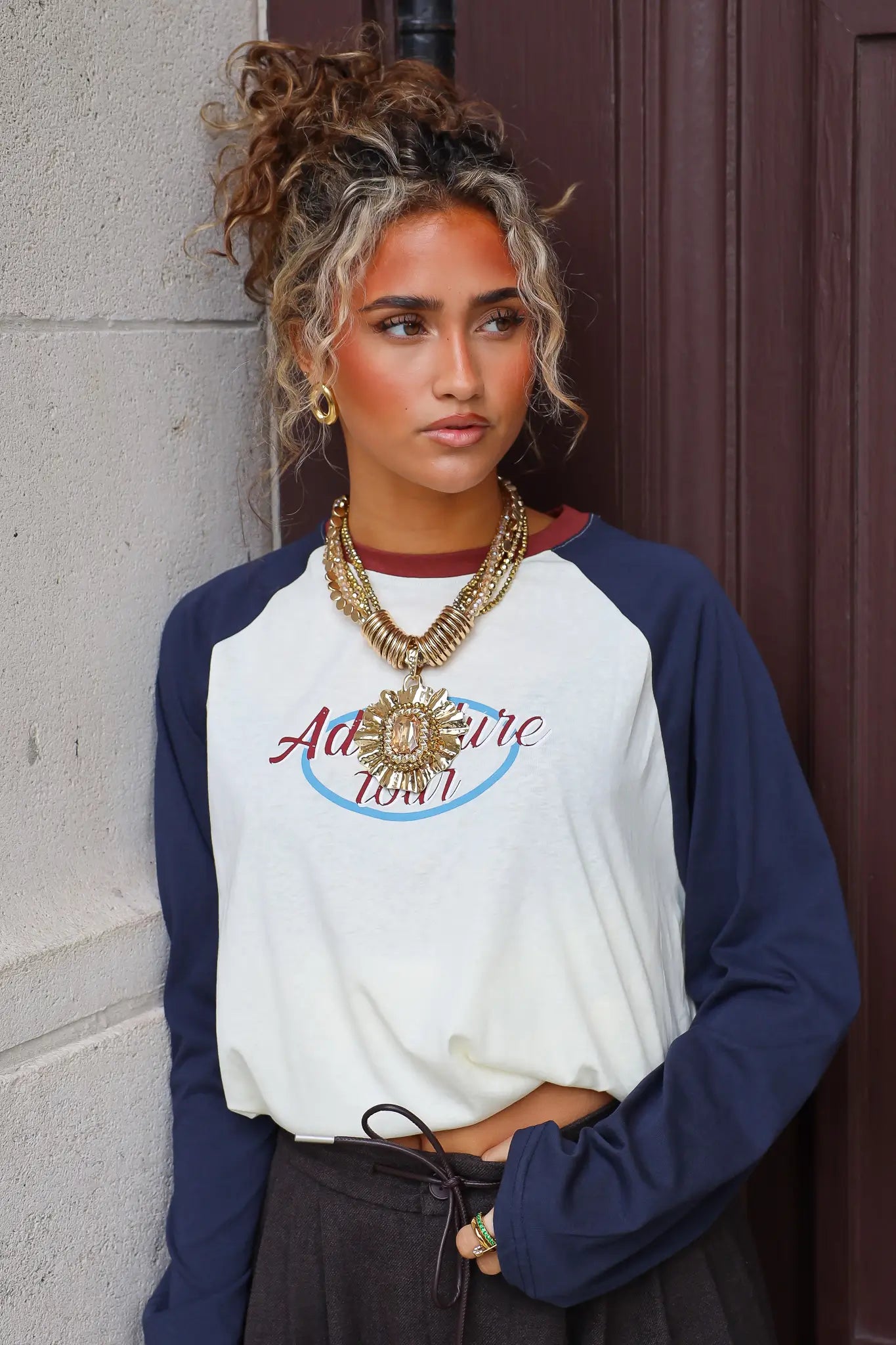Statement ketting dames goud met bloemvormige hanger en meerdere lagen gecombineerd met een shirt met donkerblauwe mouwen