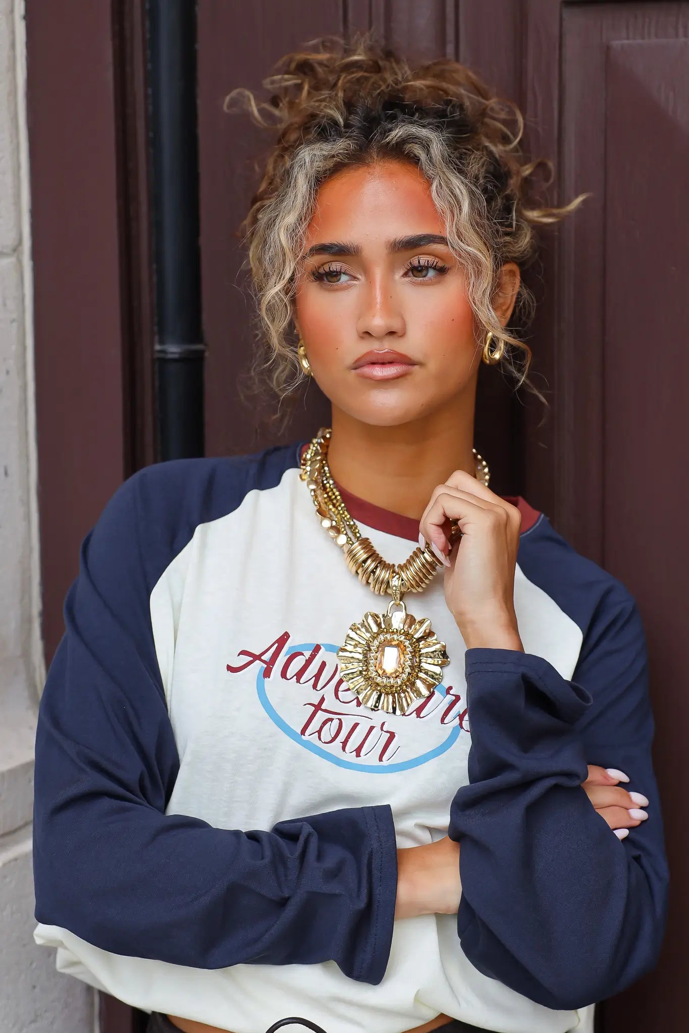 Gouden statement ketting met meerdere lagen en grote ronde hanger gedragen bij een wit shirt met donkerblauwe mouwen