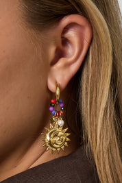 Oorbellen met zonvormige hanger gedragen aan het oor