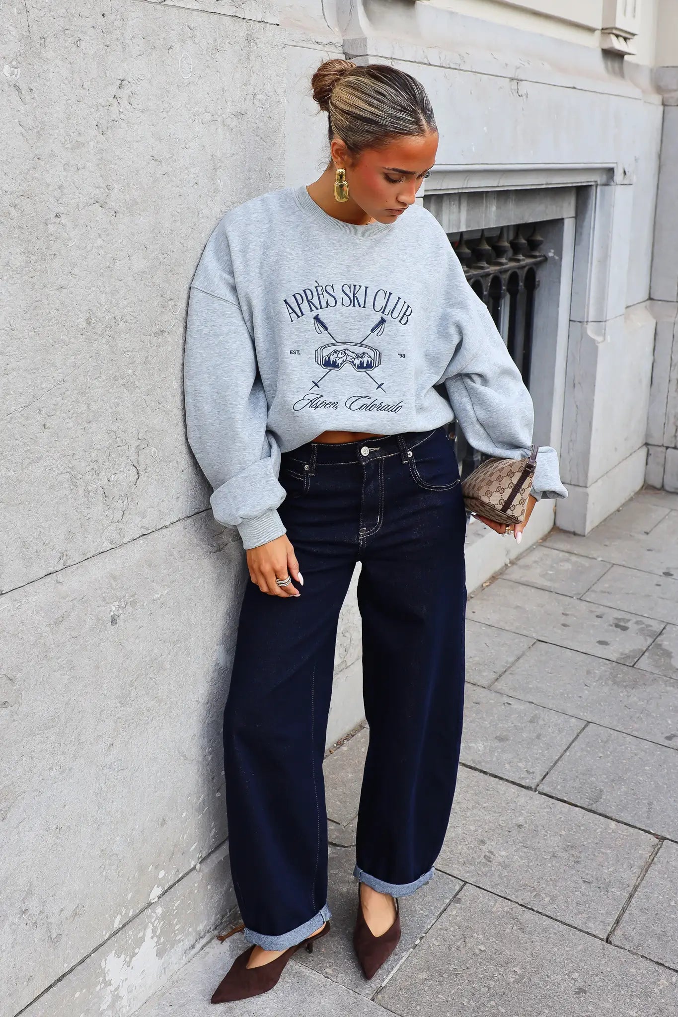 Grijze sweater met Après Ski Club opdruk gedragen met donkerblauwe wide leg jeans