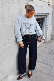 Grijze sweater met Après Ski Club opdruk gedragen met donkerblauwe wide leg jeans