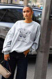 Grijze oversized Après Ski Club sweater met donkerblauwe opdruk gecombineerd met donkere jeans