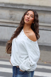 Lichtgrijze sweater met goudkleurige studs langs de brede halsopening