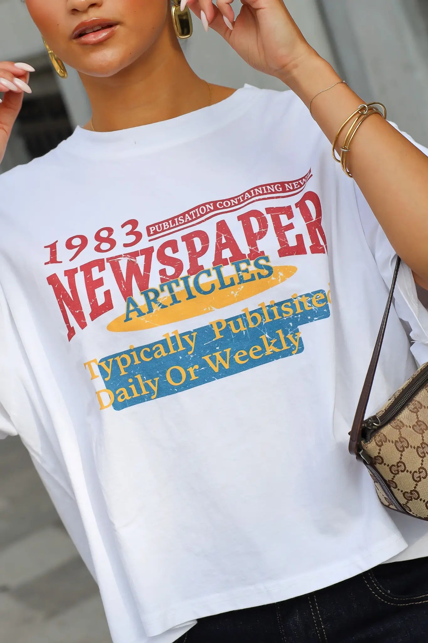 Detail van wit T-shirt met 1983 Newspaper Articles opdruk in rood geel en blauw en korte wijde mouwen