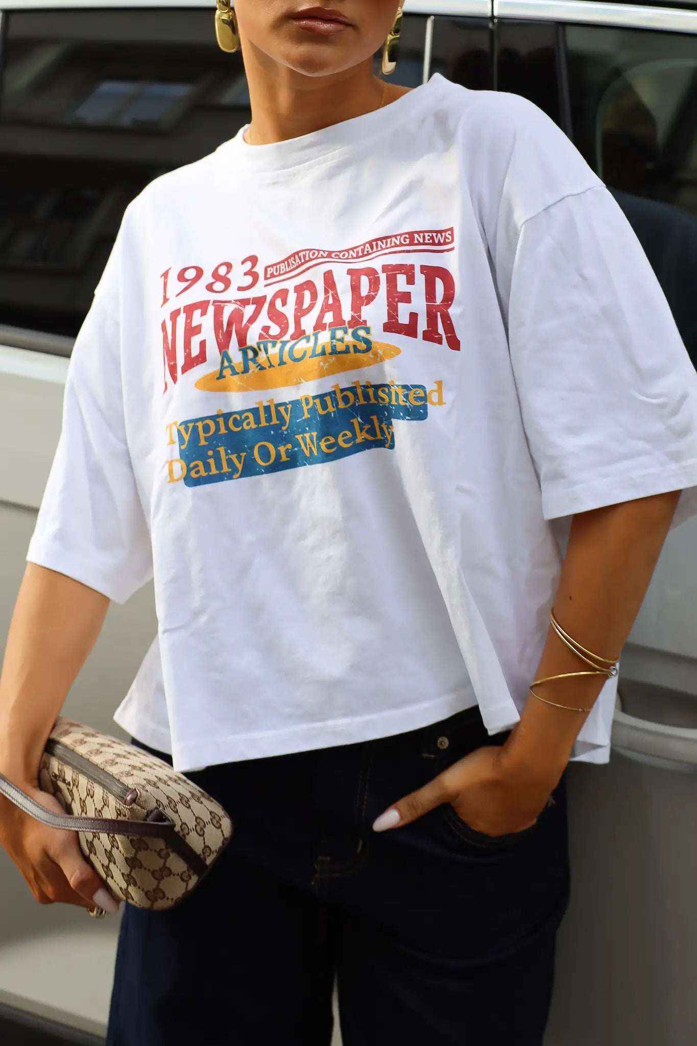 Wit oversized T-shirt met rode gele en blauwe newspaper print gedragen met een donkere jeans en beige schoudertas