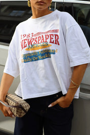 Wit oversized T-shirt met rode gele en blauwe newspaper print gedragen met een donkere jeans en beige schoudertas