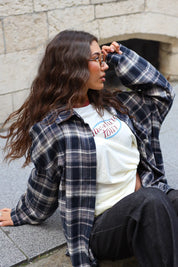 Detail van de crème Adventure longsleeve onder een donkerblauwe geruite blouse, gestyled met een zwarte broek.
