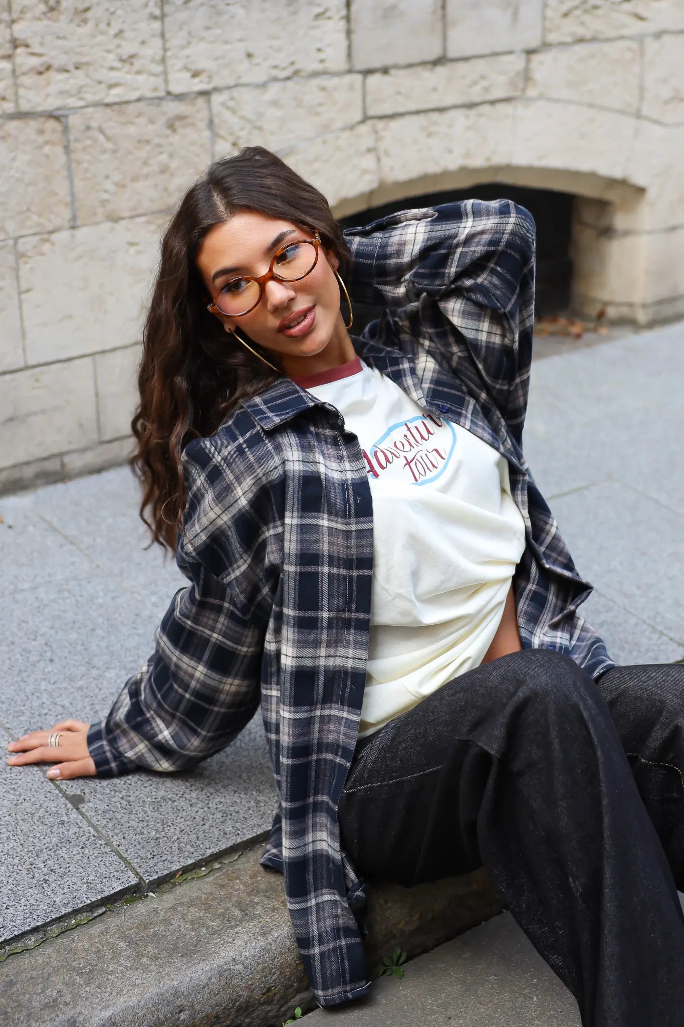 Crème longsleeve T-shirt met Adventure-print, gestyled onder een open geruite blouse met donkere jeans.