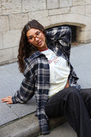 Crème longsleeve T-shirt met Adventure-print, gestyled onder een open geruite blouse met donkere jeans.