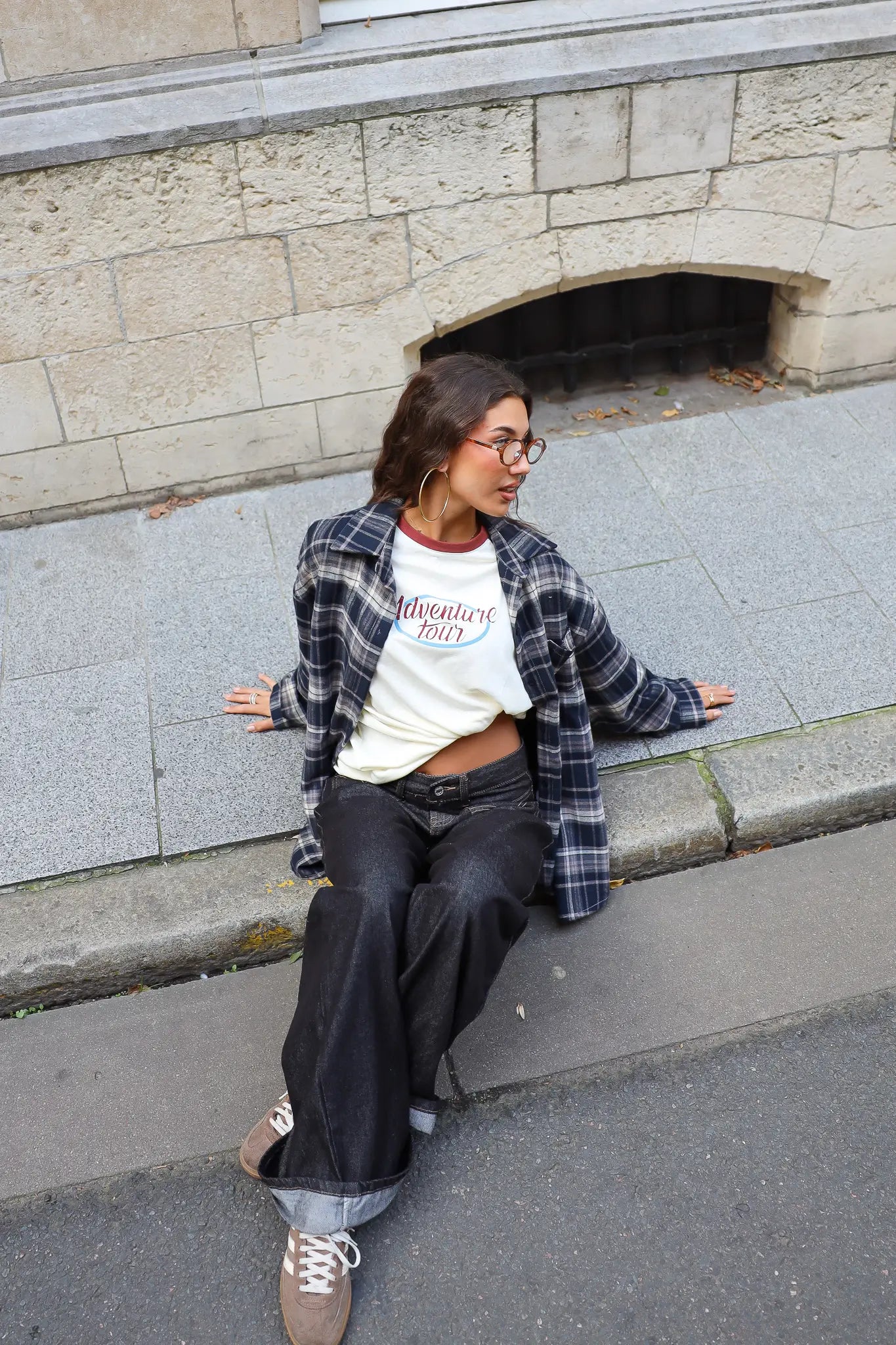 Crème Adventure longsleeve gecombineerd met een open donkerblauwe geruite blouse en zwarte wide leg jeans in een casual streetstyle outfit.
