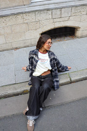 Crème Adventure longsleeve gecombineerd met een open donkerblauwe geruite blouse en zwarte wide leg jeans in een casual streetstyle outfit.