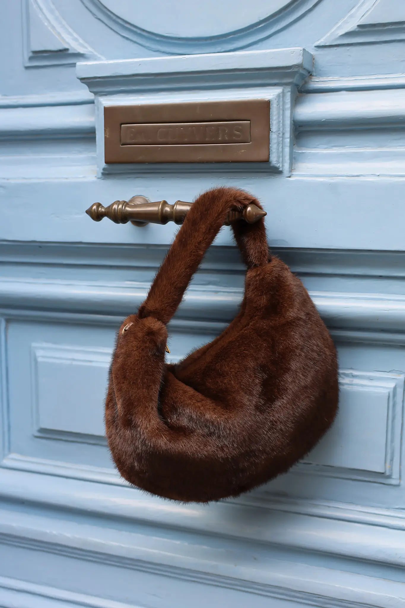 Donkerbruine faux fur schoudertas van zacht imitatiebont met kort hengsel hangend aan blauwe deur