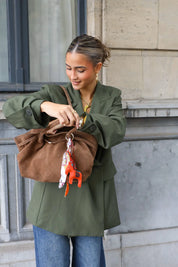 vrouw met taupe suède shopper in hand bij stenen muur