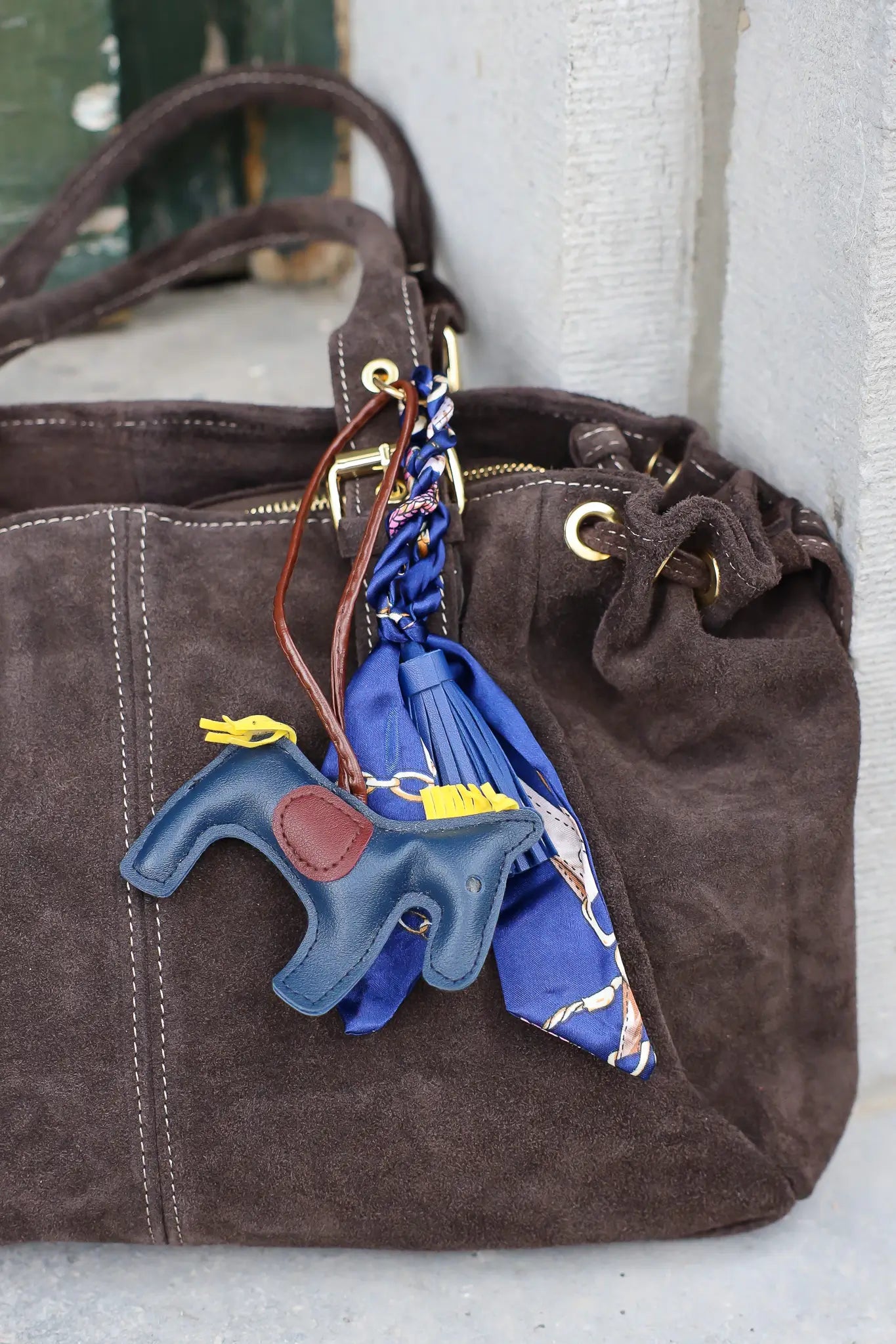 close-up van donkerbruine suède tas met blauwe sjaal aan hengsel