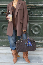 vrouw draagt donkerbruine suède tas met verstelbare koorden bij groene deur