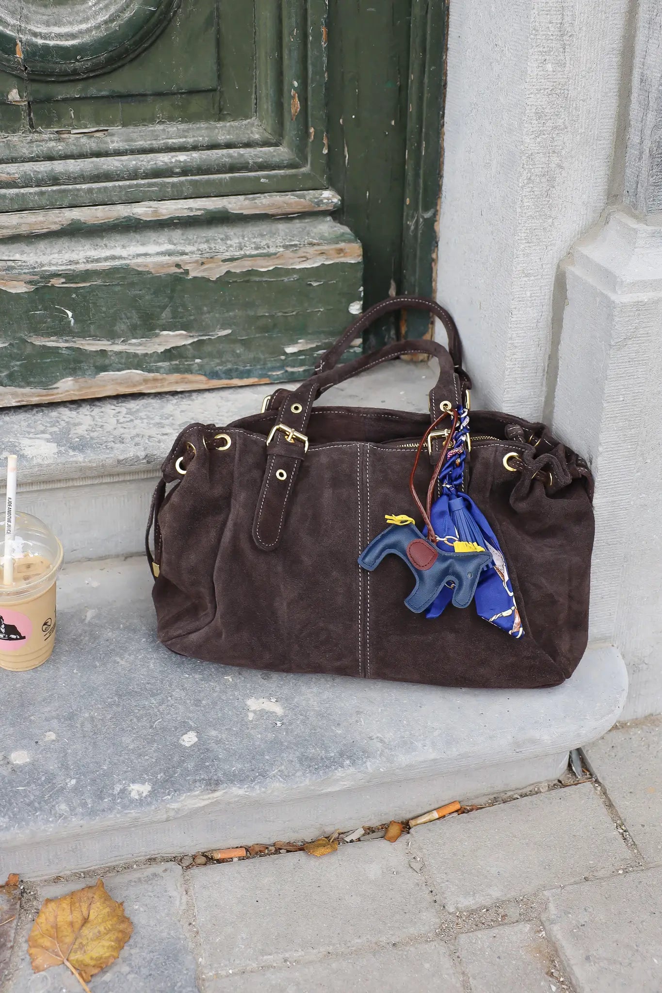 donkerbruine suède handtas groot formaat gefotografeerd buiten bij groene deur