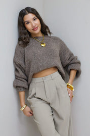 Model draagt taupe fluffy trui iets opgetrokken boven beige pantalon