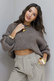 Model poseert met licht opgetrokken taupe fluffy trui en beige pantalon