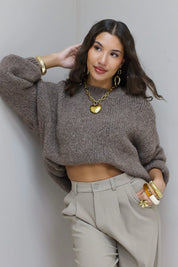 Model met hand in het haar draagt taupe fluffy trui met beige pantalon
