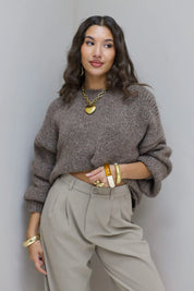 Model draagt taupe fluffy trui met beige pantalon en gouden ketting