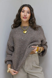 Model staat recht met handen in zakken in taupe fluffy trui en beige broek