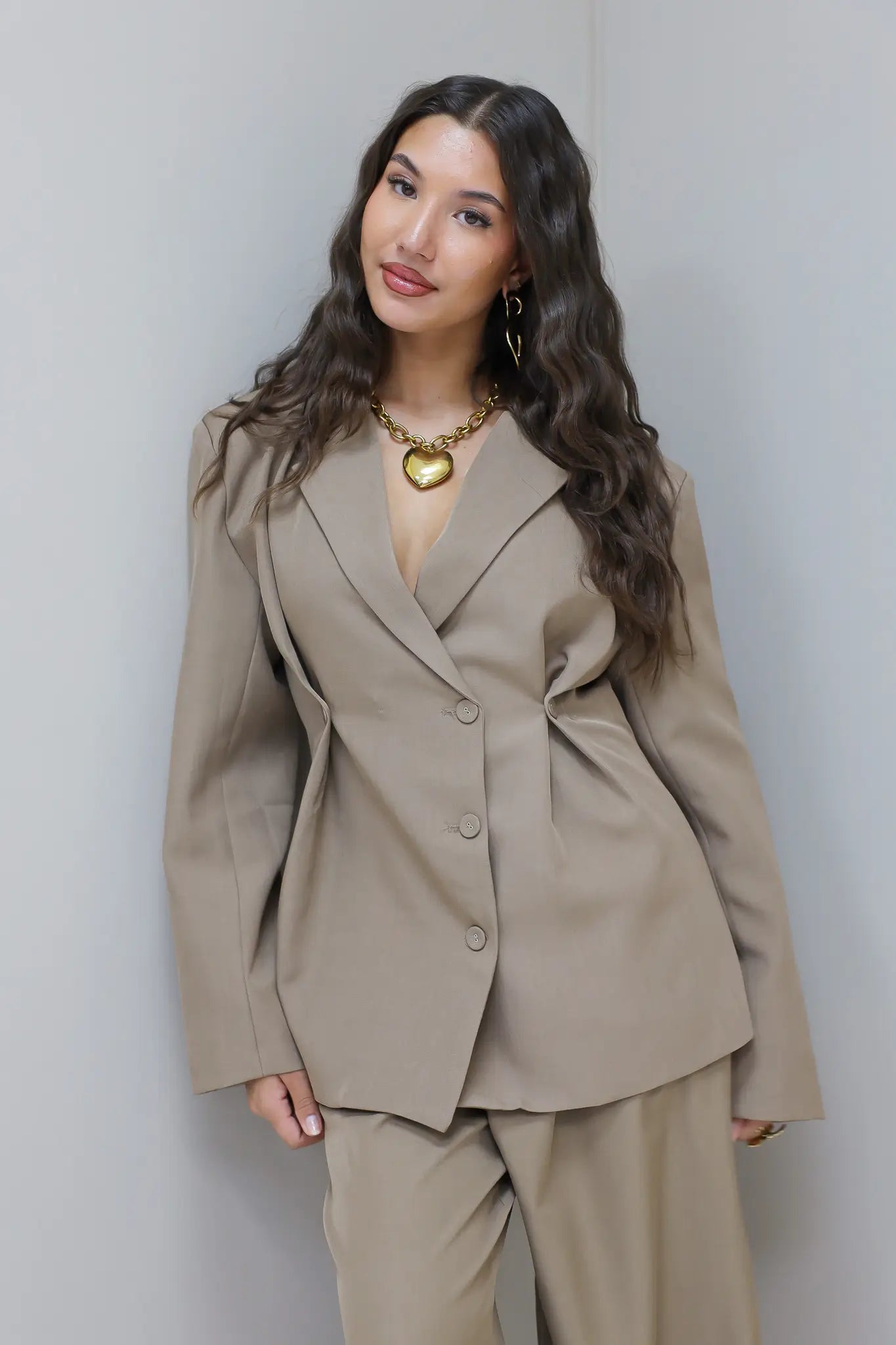 Model staat recht met taupe blazer en pantalon