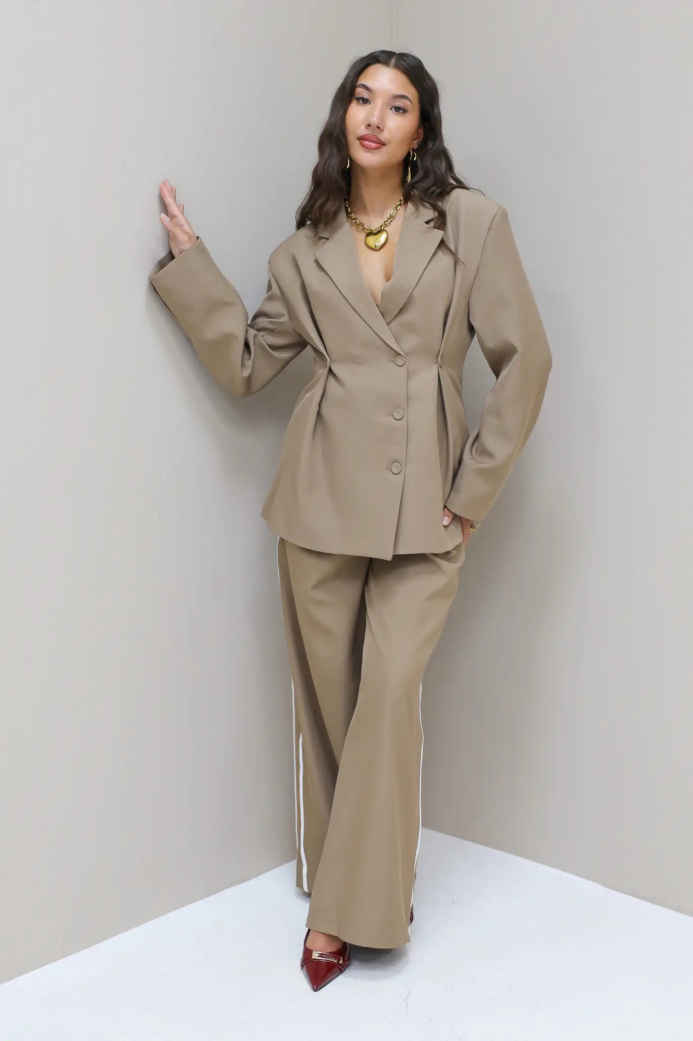 Model stapt zijwaarts in taupe blazer met pantalon en hakken