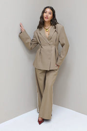 Model stapt zijwaarts in taupe blazer met pantalon en hakken