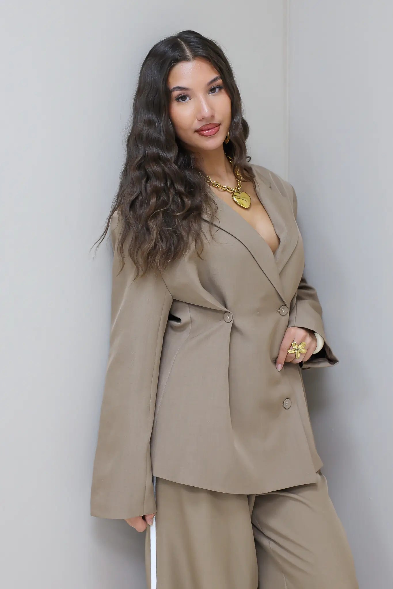 Model poseert in taupe blazer met pantalon bij lichte wand