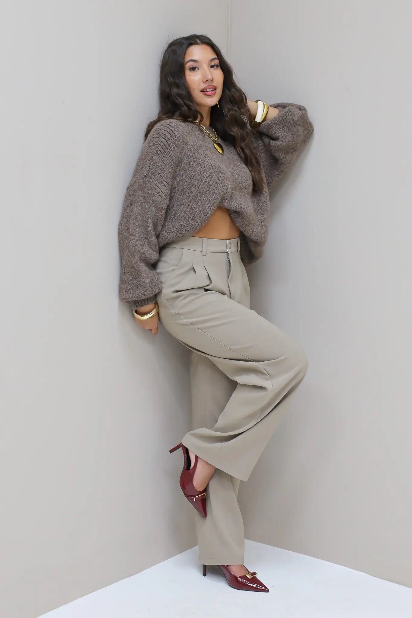 Model draagt taupe pantalon met grijze trui en hakken