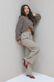Model draagt taupe pantalon met grijze trui en hakken