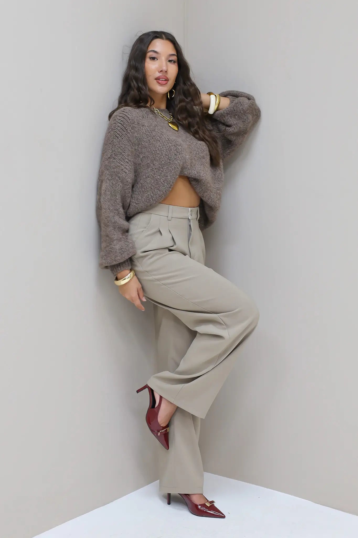 Model staat in hoek met taupe pantalon en grijze trui