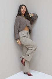 Model staat in hoek met taupe pantalon en grijze trui