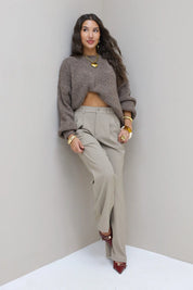 Model poseert in taupe pantalon met grijze trui en rode hakken