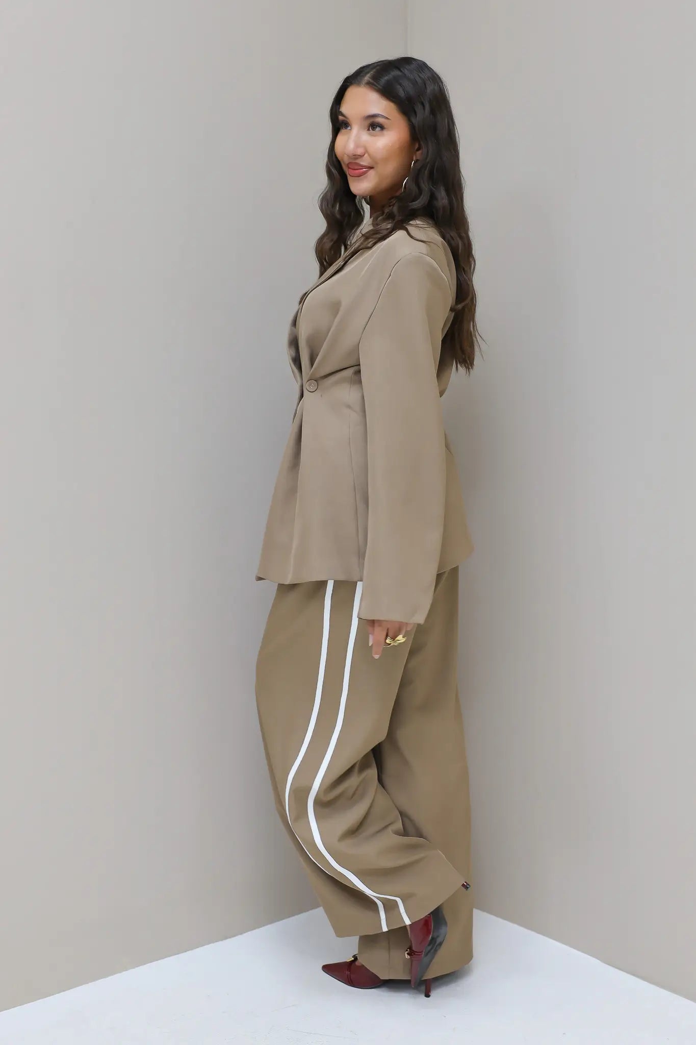 Model kijkt over schouder met taupe pantalon met witte bies