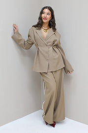 Model leunt tegen muur met taupe pantalon met witte bies