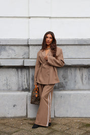 Model draagt taupe pantalon met witte bies en bruine blazer op straat