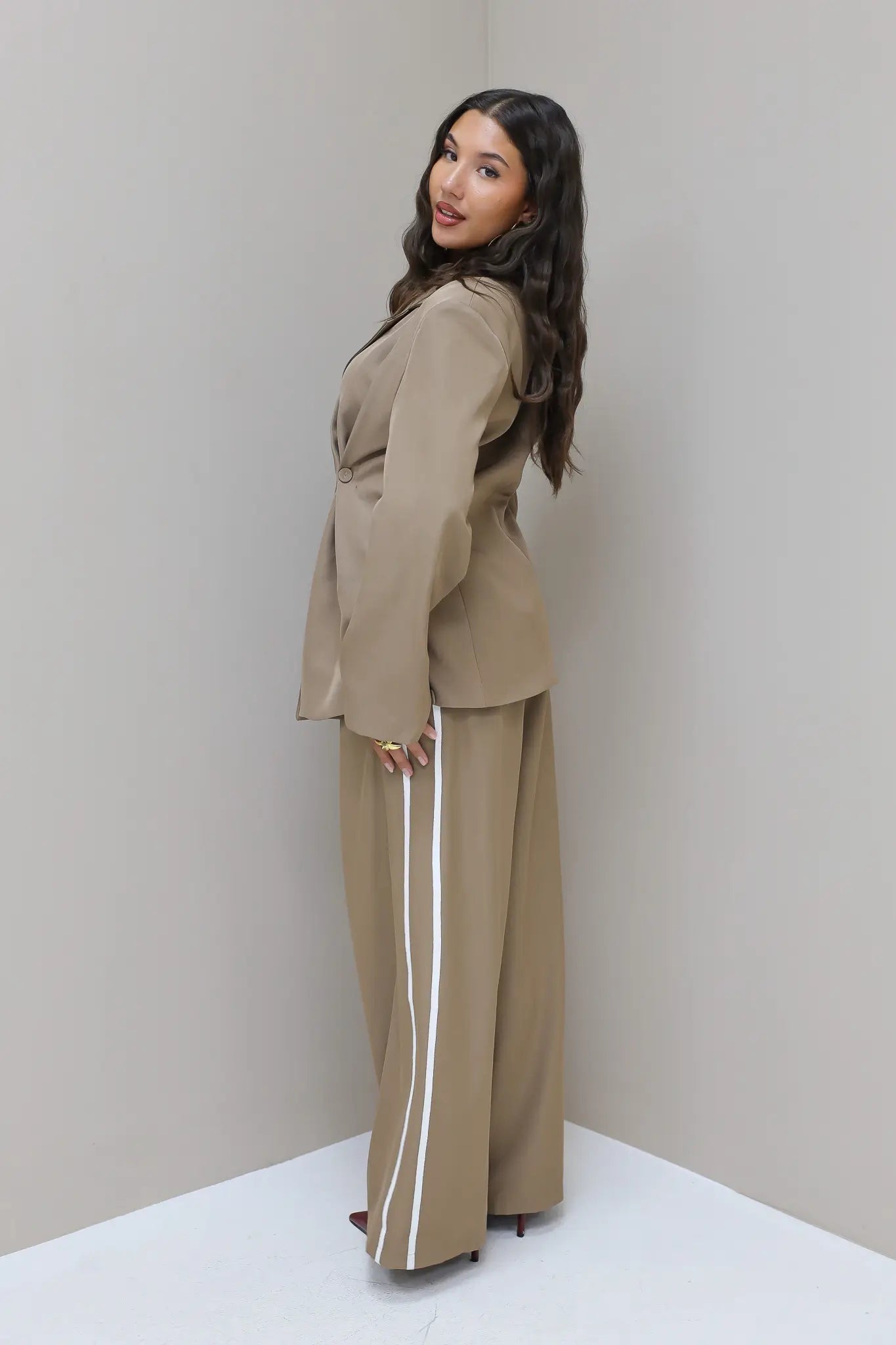 Model poseert in studio met taupe pantalon met witte bies