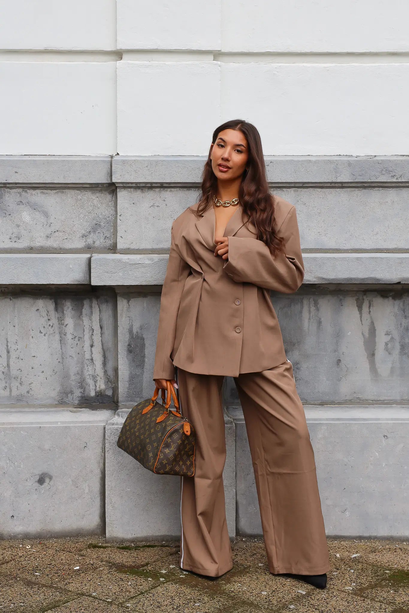 Model draagt taupe pantalon met witte bies en handtas