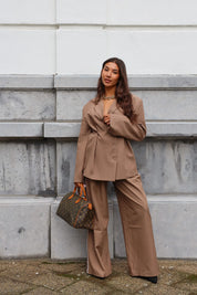 Model draagt taupe pantalon met witte bies en handtas