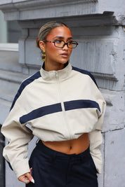 Close-up van camel track jacket met hoge ritssluiting opstaande kraag en brede donkerblauwe streep op de borst
