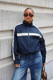 Close-up van donkerblauw track jacket met beige streep over de borst hoge kraag en ritssluiting