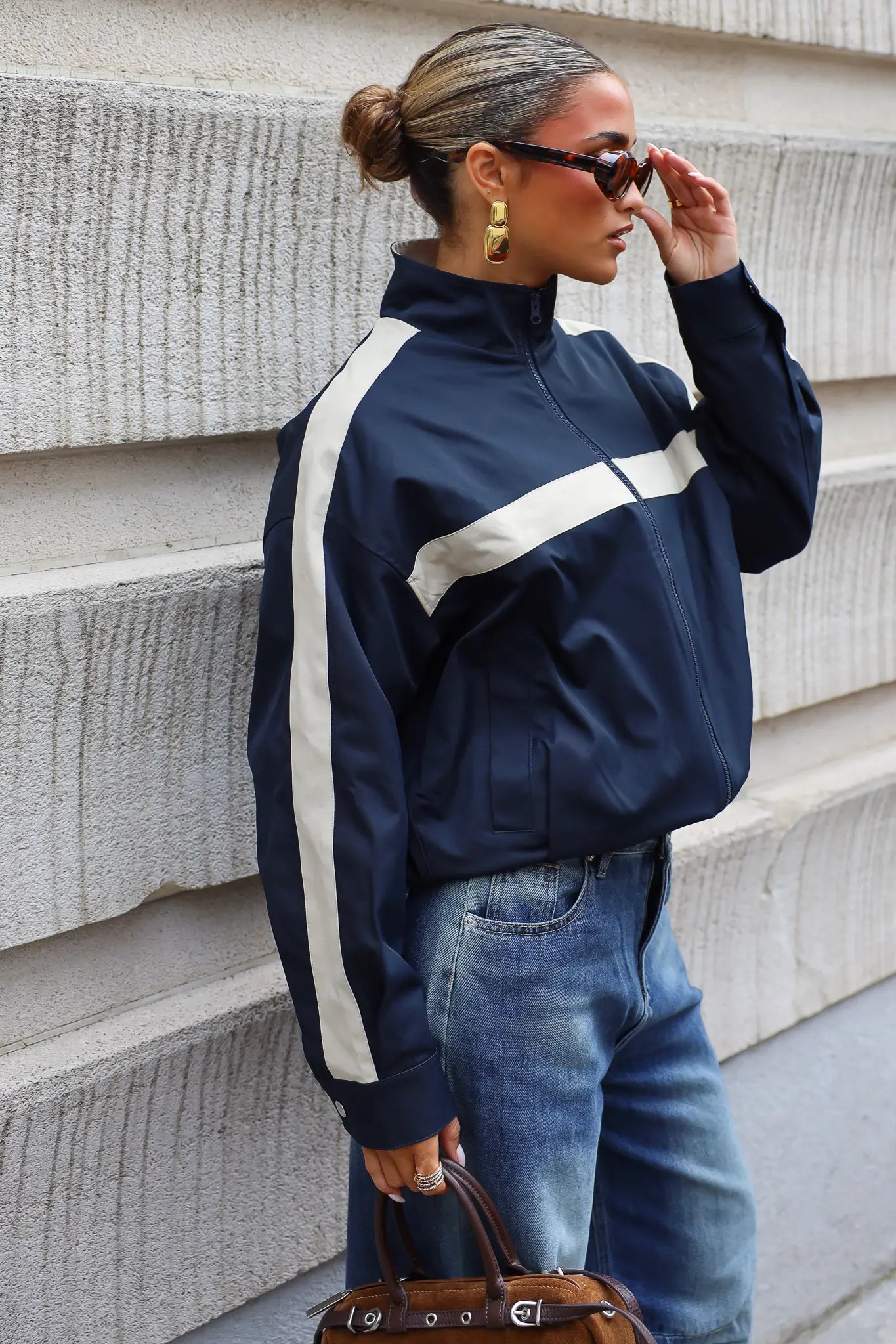 Donkerblauwe track jas dames met hoge kraag beige strepen en ritssluiting gecombineerd met een blauwe wide leg jeans